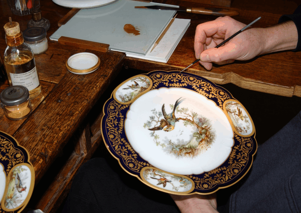 Artisan de la Manufacture de Sèvres peignant une illustration sur une assiette en porcelaine
